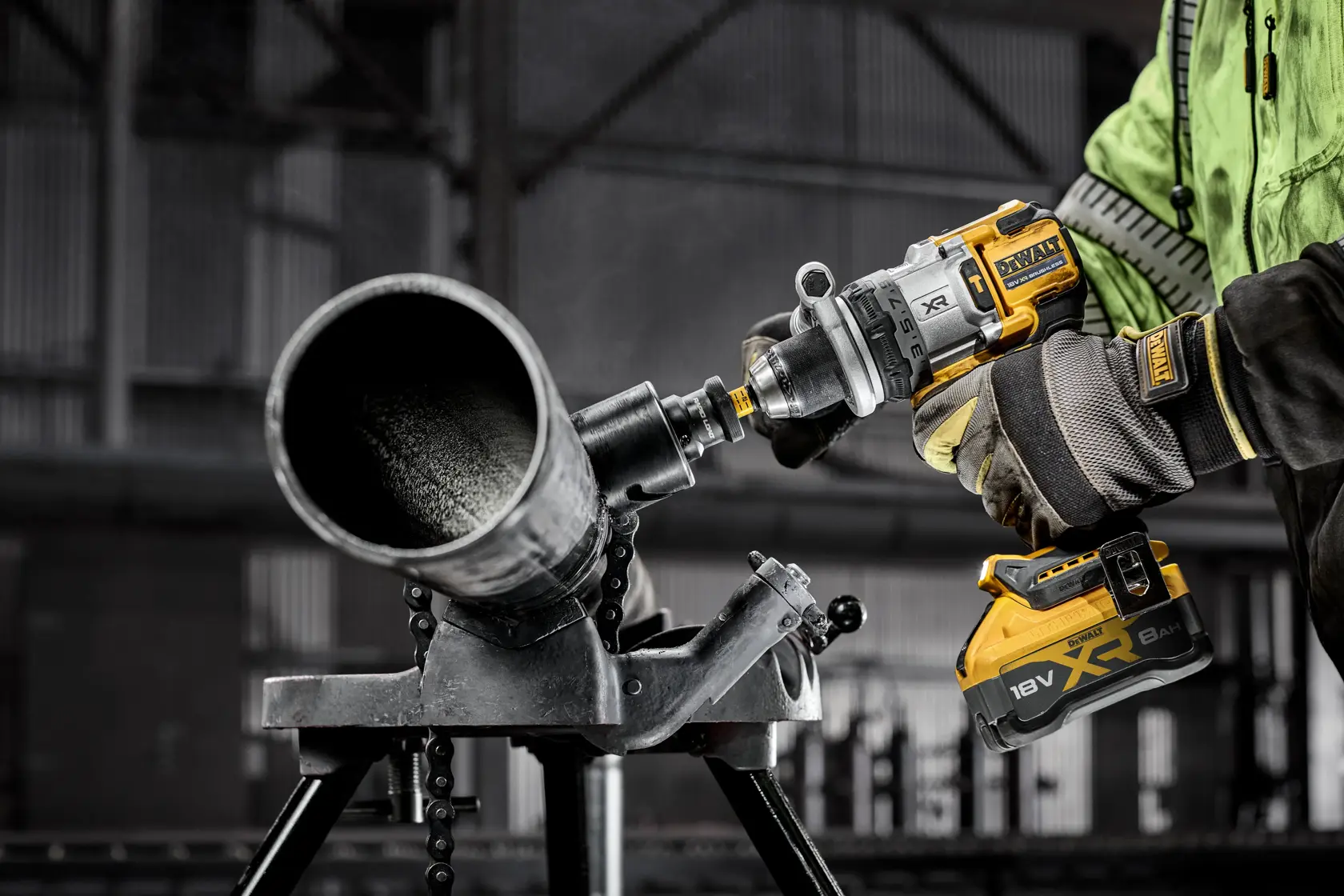 Trabajador usa herramienta DEWALT XR 18V con batería para perforar tubo metálico en entorno industrial.