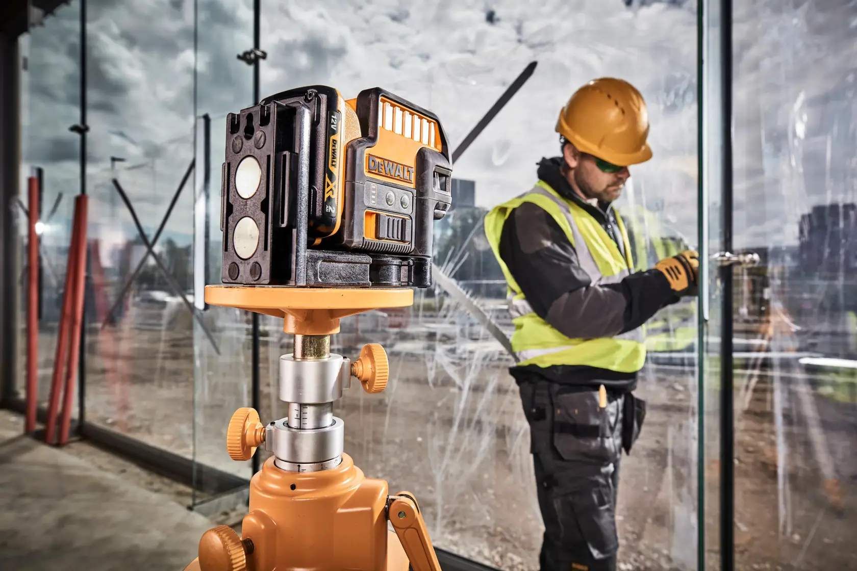 DEWALT grüner Laser auf Stativ, Bauarbeiter installiert Glasscheibe im Hintergrund.