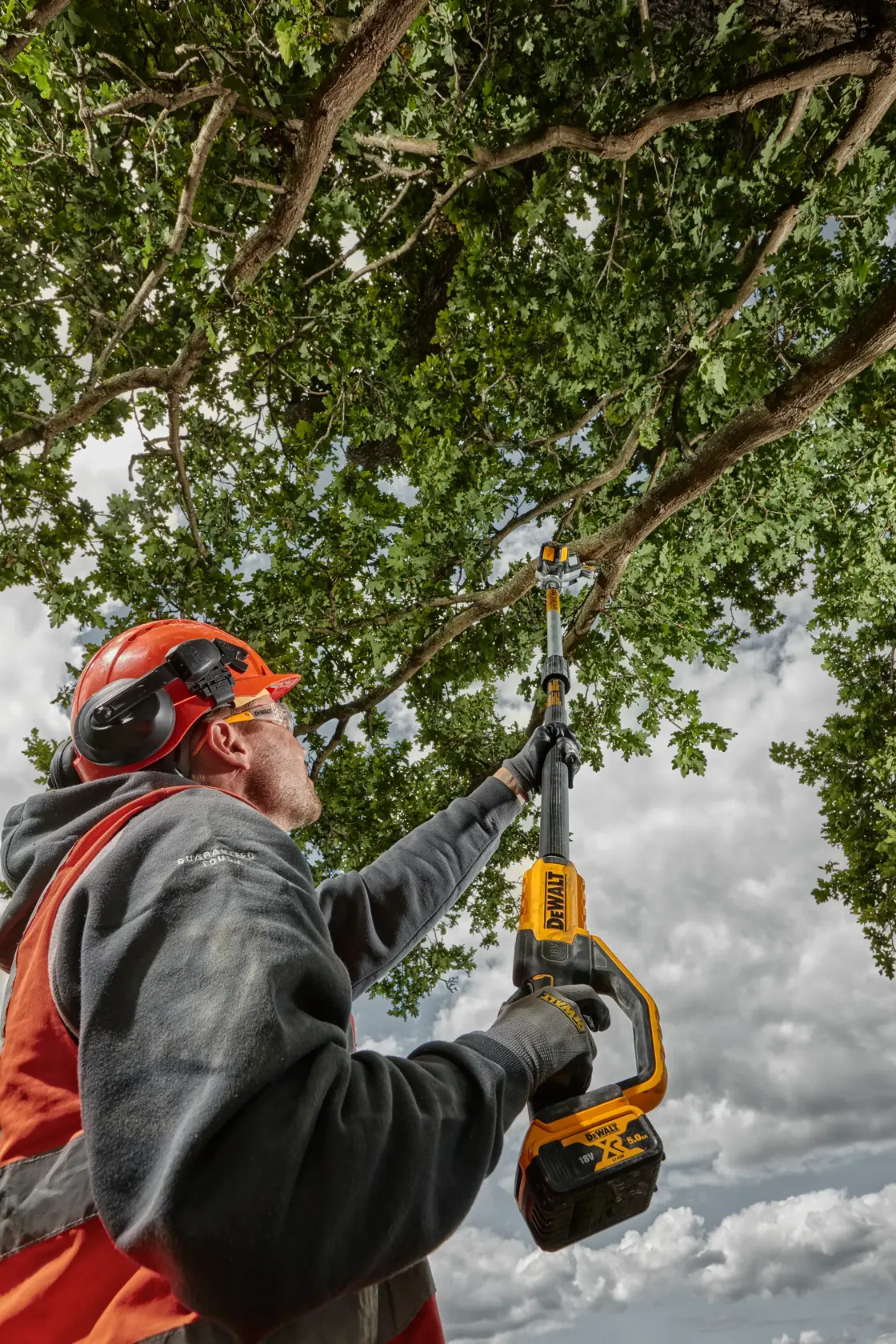Persona recorta ramas de árbol con una motosierra DEWALT inalámbrica, usando equipo de seguridad.