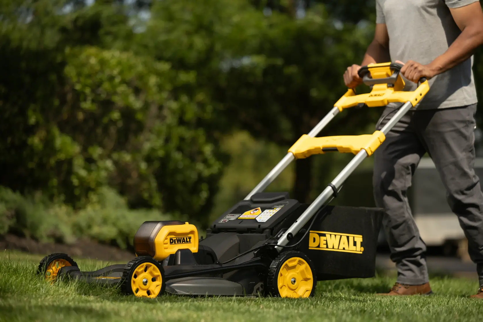 Personne utilisant une tondeuse sans fil DEWALT sur de l’herbe, vue rapprochée du guidon et de la tondeuse.