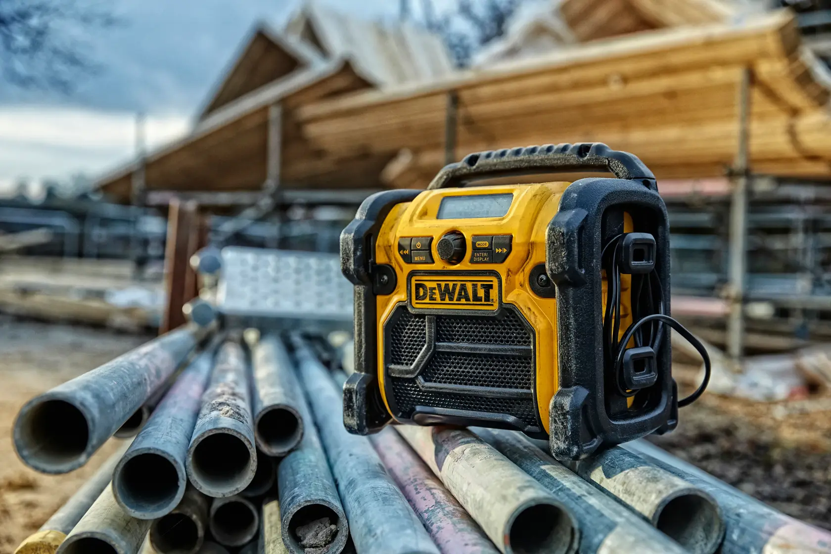 DEWALT DCR020 Radio auf Metallrohren an einer Baustelle, Holzkonstruktion im Hintergrund.