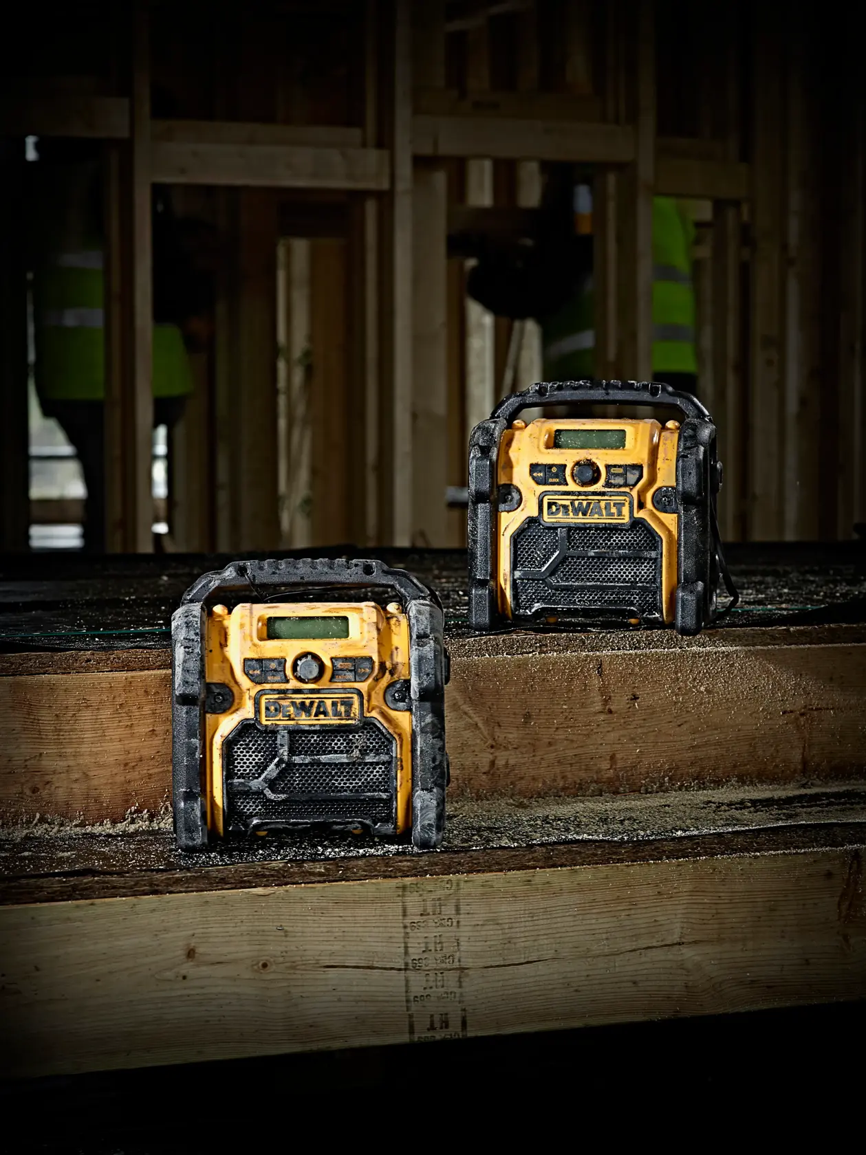 Zwei DEWALT DCR020-Radios auf einer Baustelle, auf Holzbalken platziert.