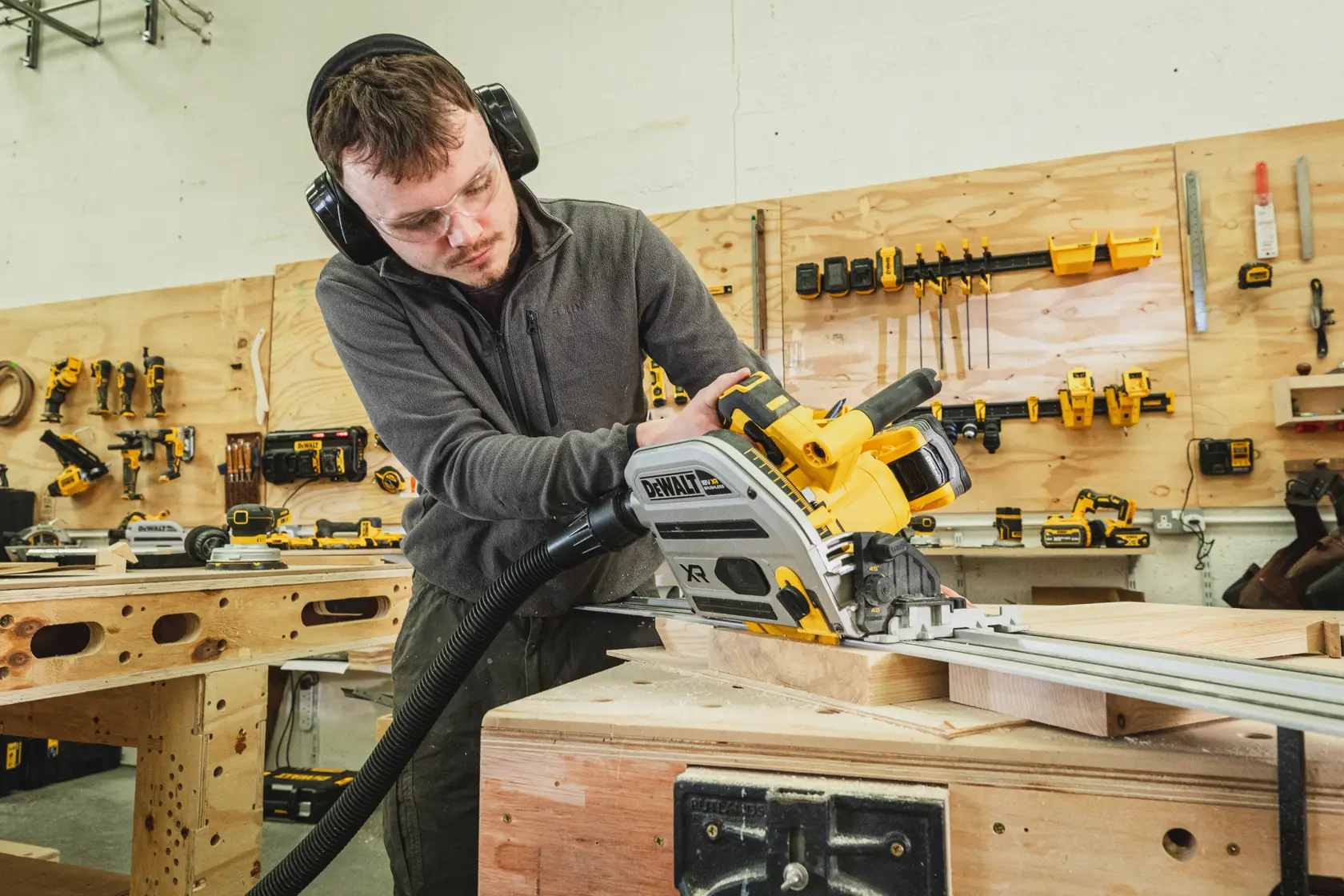 Person sägt Holz mit einer DEWALT Führungsschiene in einer Werkstatt. Werkzeuge sind an der Wand sichtbar.
