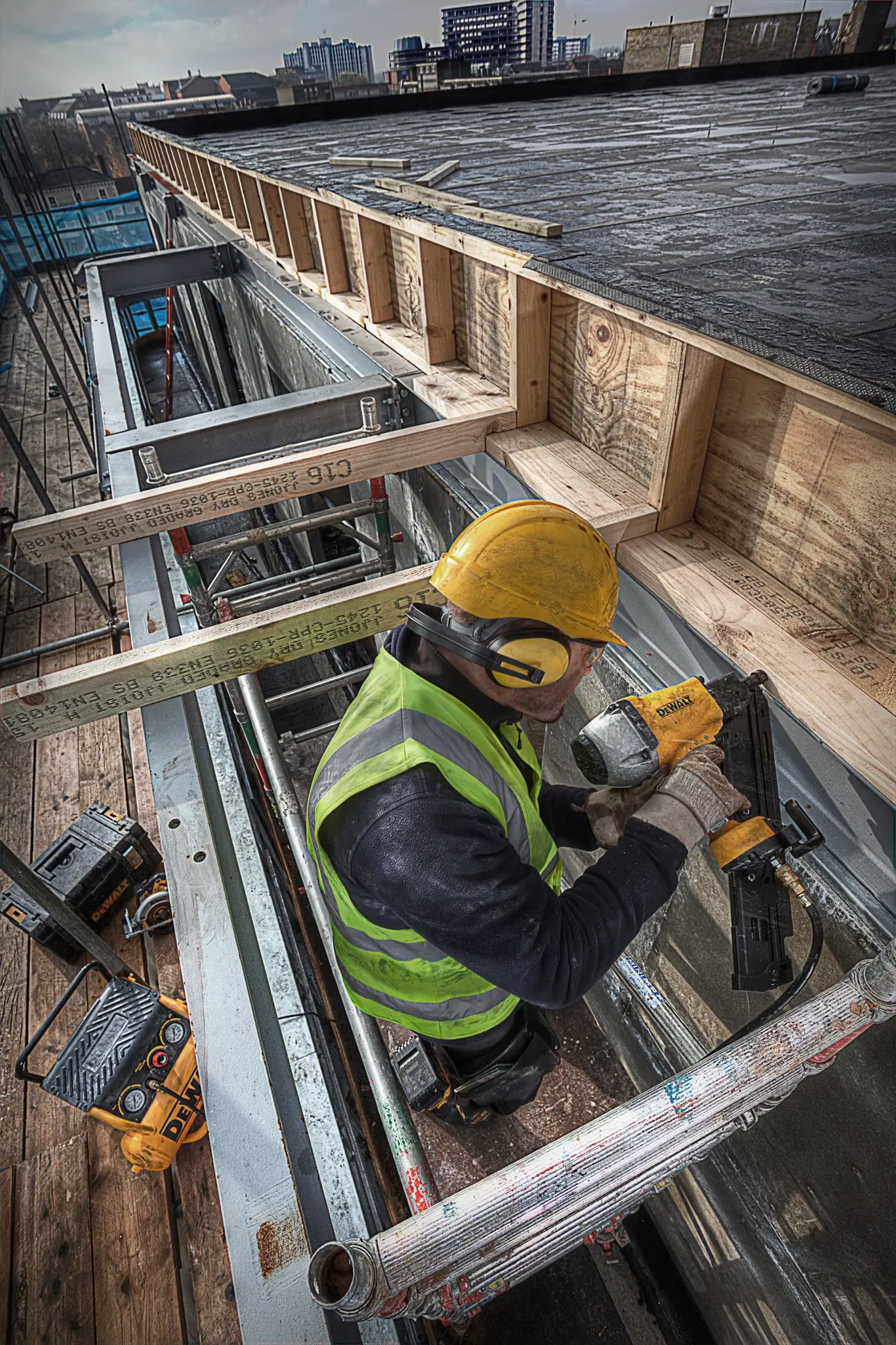 Arbeiter nutzt DEWALT Nagelpistole auf Baustelle mit Schutzkleidung und Holzträgern.