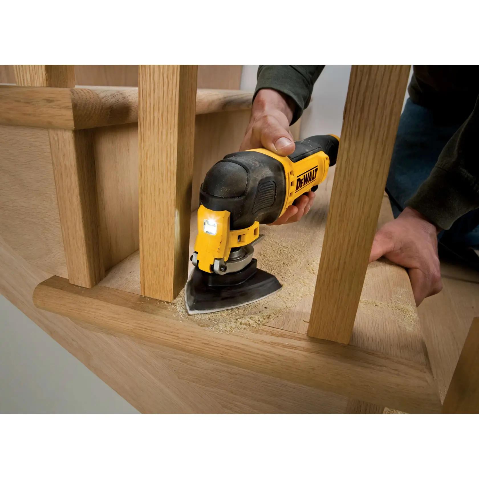 Multitool DEWALT lijando madera en escalera. Serrín visible. Persona sostiene herramienta, área de trabajo cerca.
