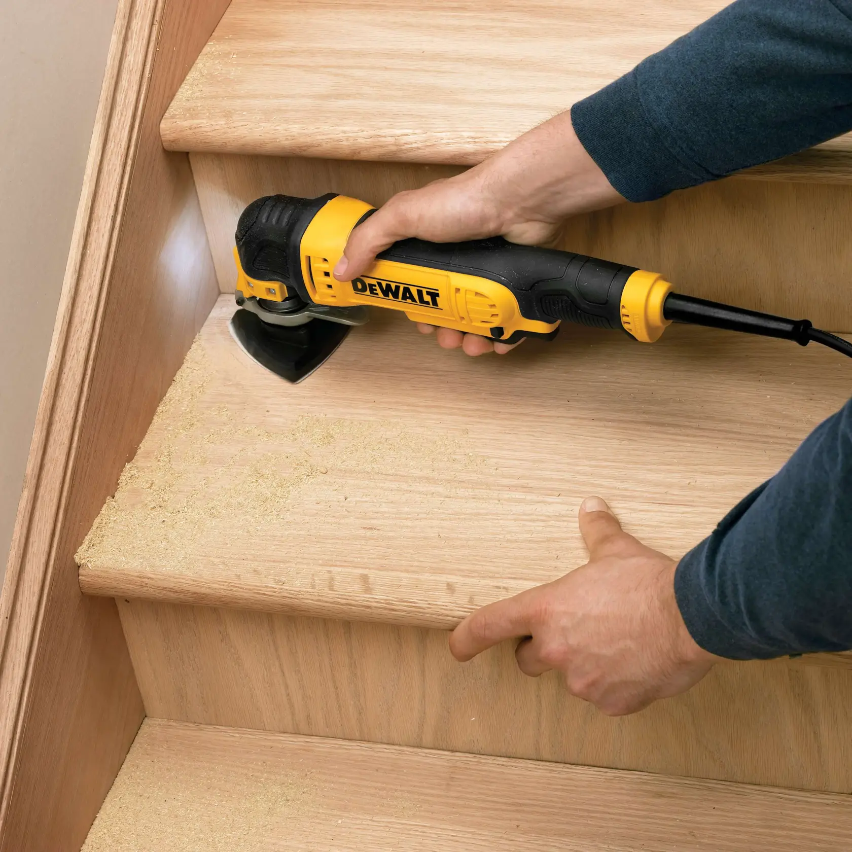 Una lijadora DEWALT se usa en una escalera de madera, generando polvo de madera al lijar.