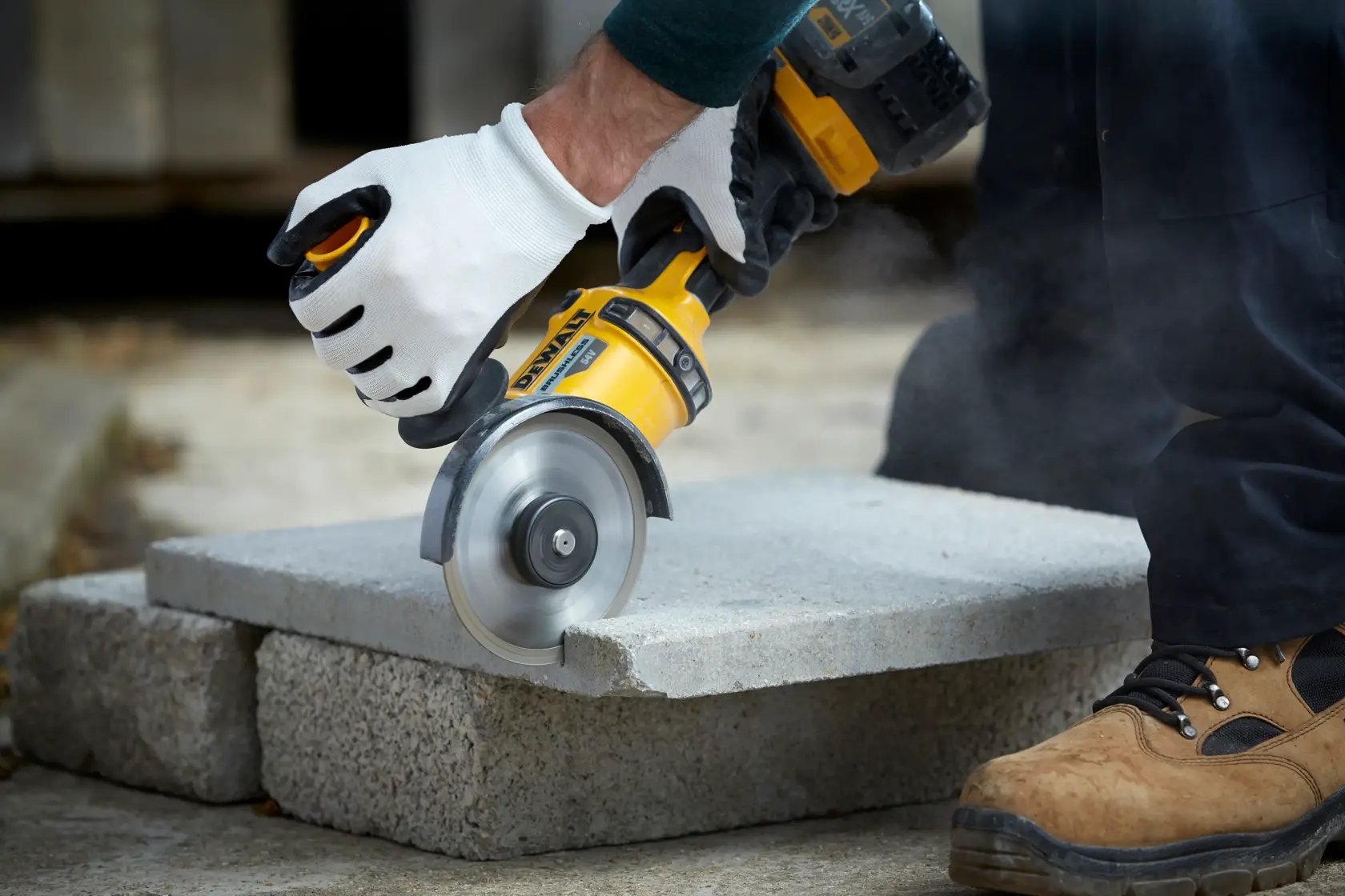 Person schneidet Betonblock mit DEWALT Werkzeug, trägt Handschuhe und Arbeitsschuhe im Freien.