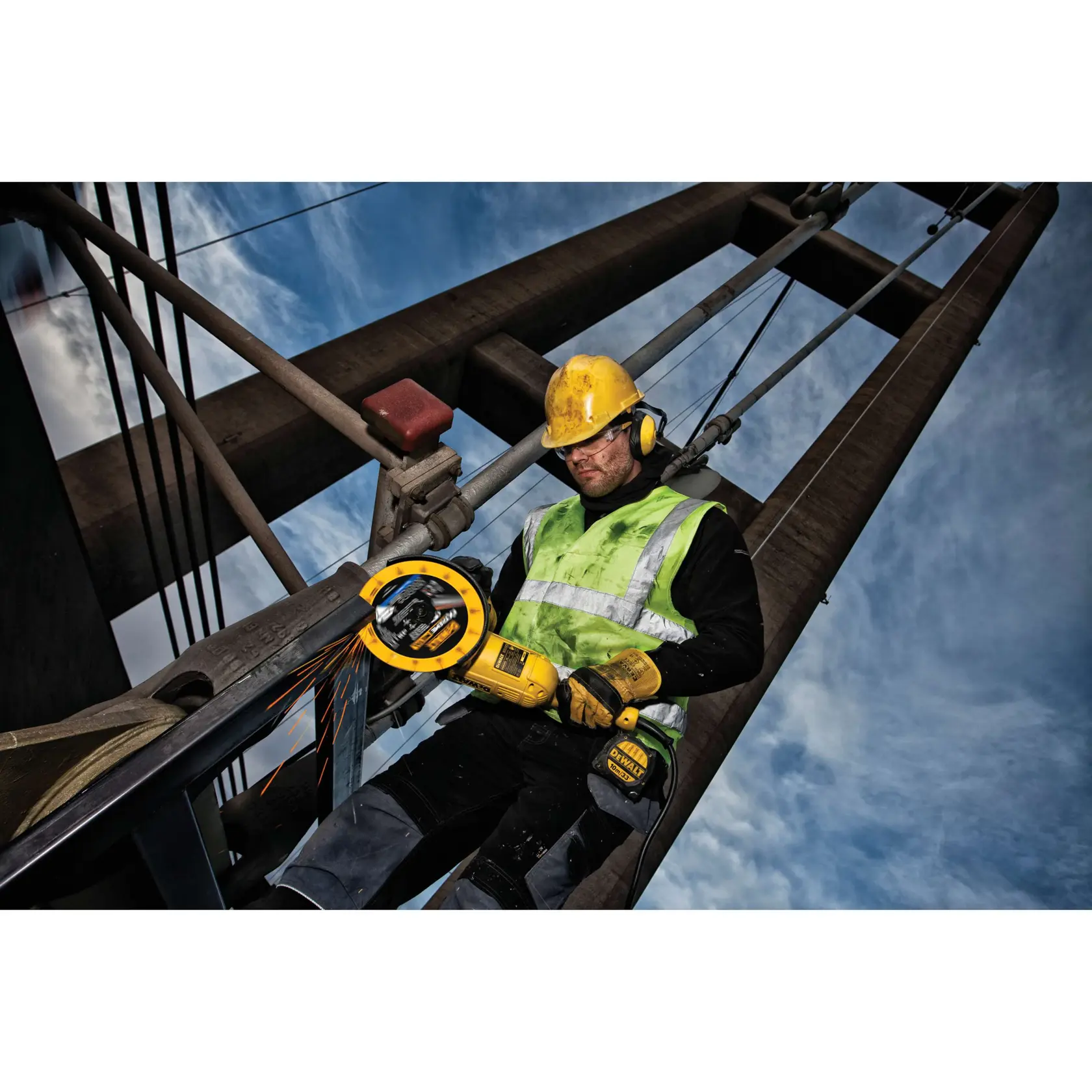 Trabajador usa amoladora DEWALT en estructura metálica al aire libre, con equipo de seguridad.
