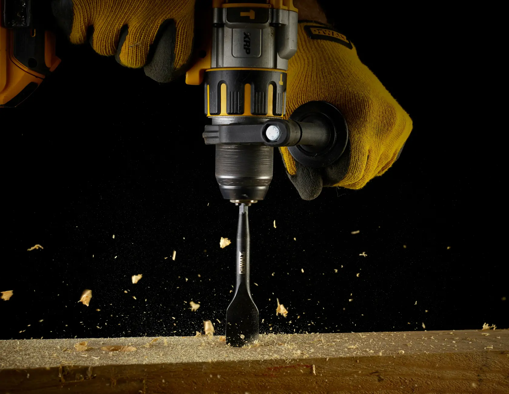 DEWALT-Bohrmaschine mit Schaufelbohrer bohrt Holz, Sägemehl fliegt, behandschuhte Hände halten das Werkzeug.