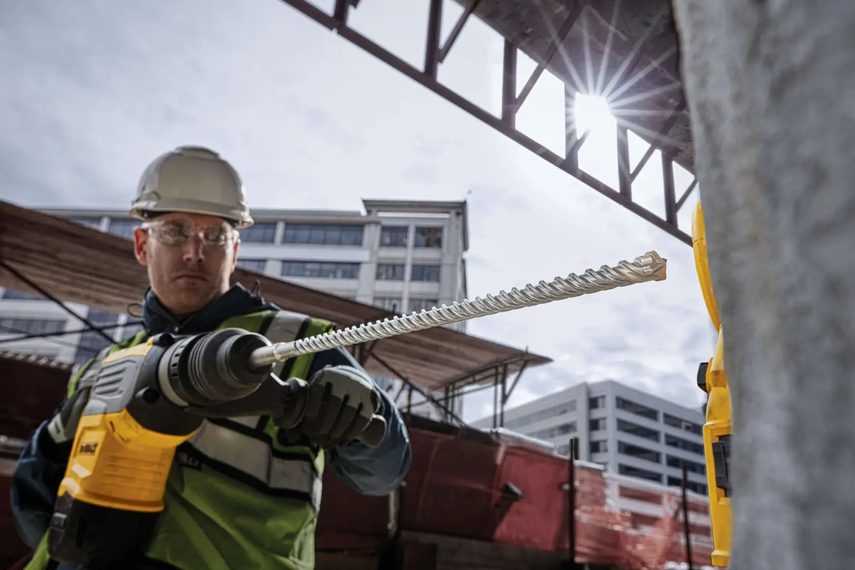 Arbeiter mit DEWALT DT60810 Bohrer auf Baustelle, Gebäude im Hintergrund.