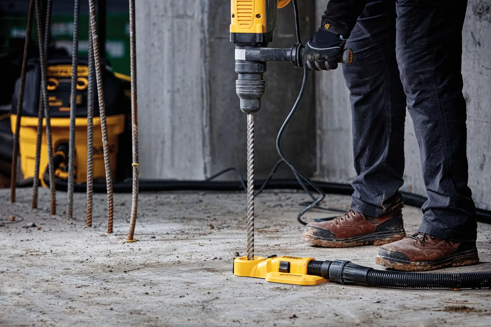 Arbeiter benutzt DEWALT-Bohrmaschine mit langem Bohrer auf Baustelle, Gebäude im Hintergrund.