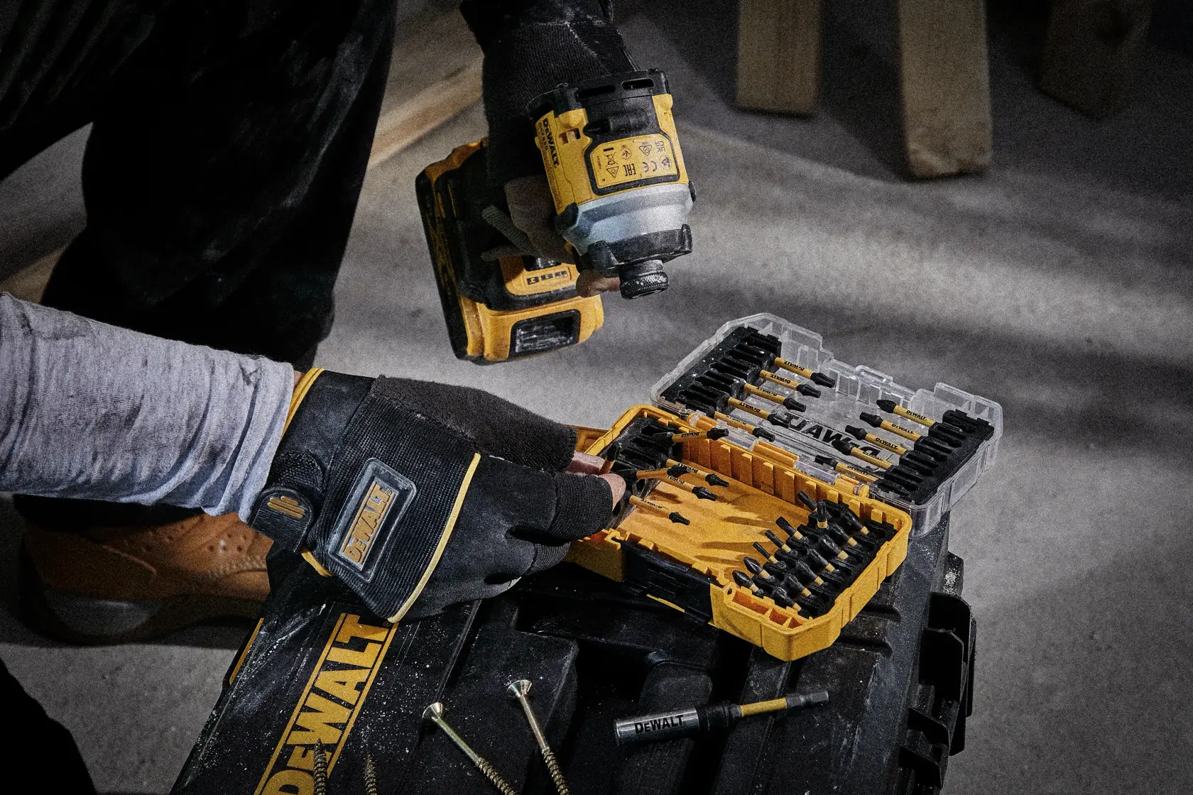 Person nutzt DEWALT-Bohrmaschine an Holzplatte auf Baustelle, mit Schutzkleidung und Handschuhen.