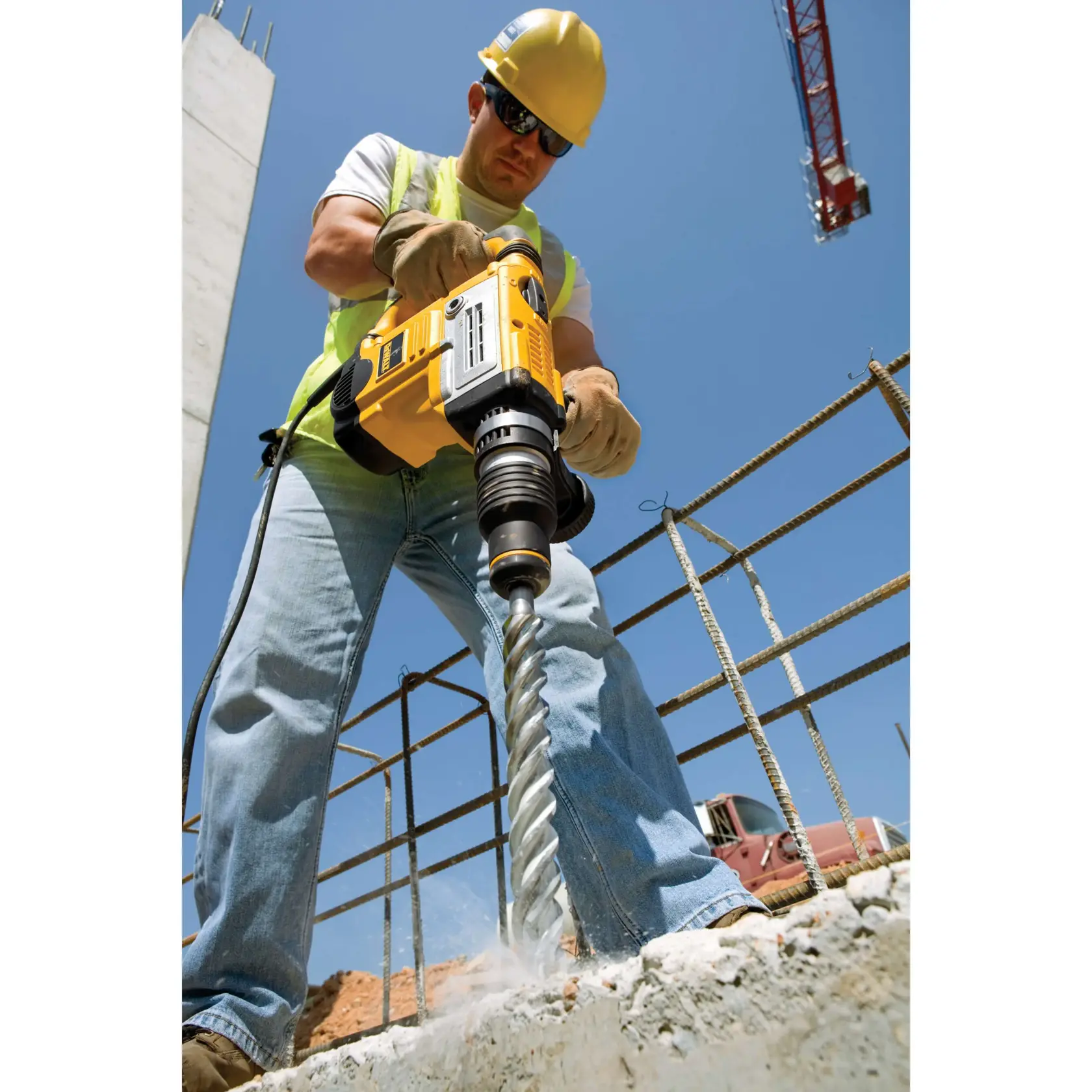 Arbeiter bohrt mit DEWALT-Bohrer in Beton, trägt Schutzkleidung und Handschuhe auf Baustelle.