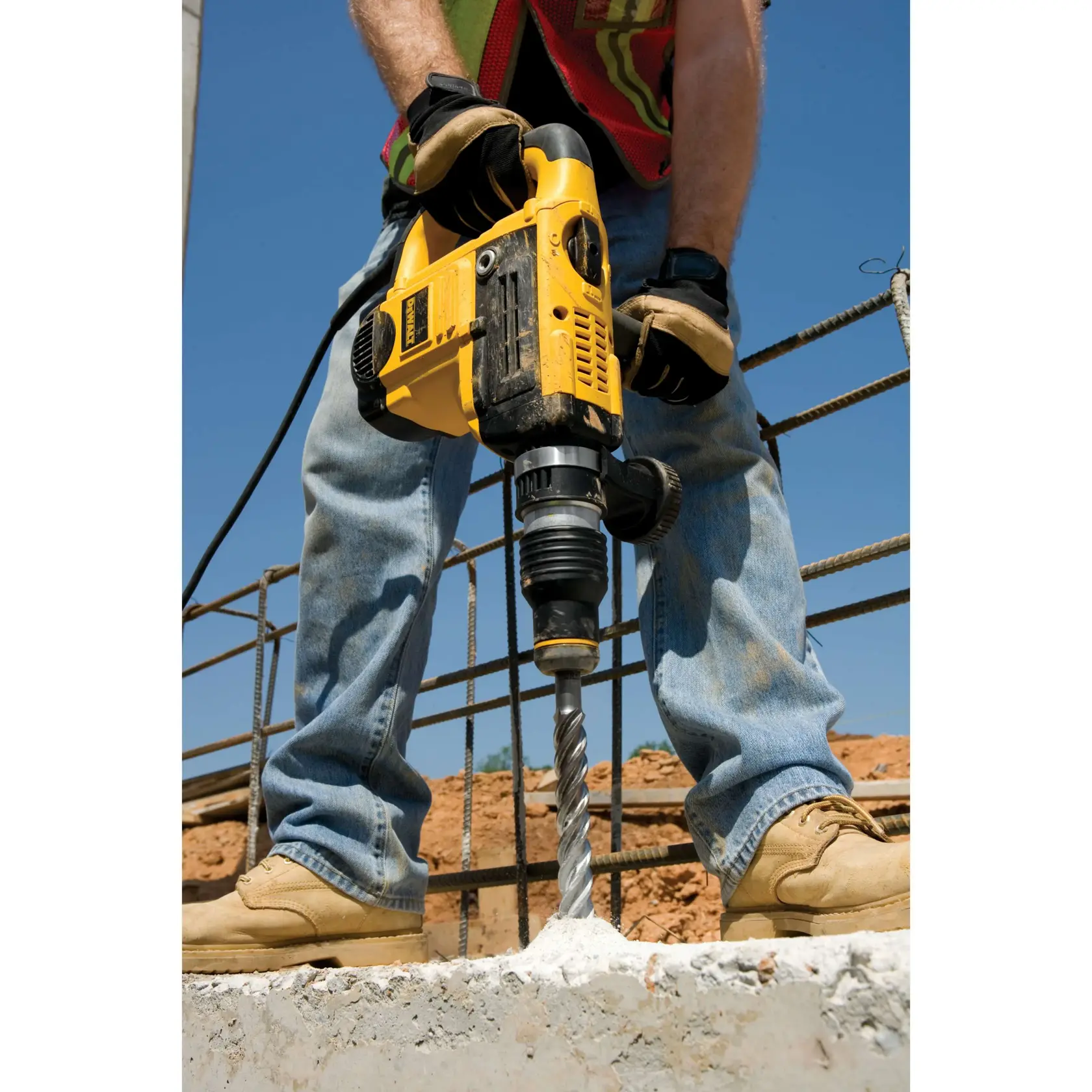 Person bohrt mit DEWALT-Bohrmaschine in Beton auf Baustelle und trägt Handschuhe und Arbeitsschuhe.