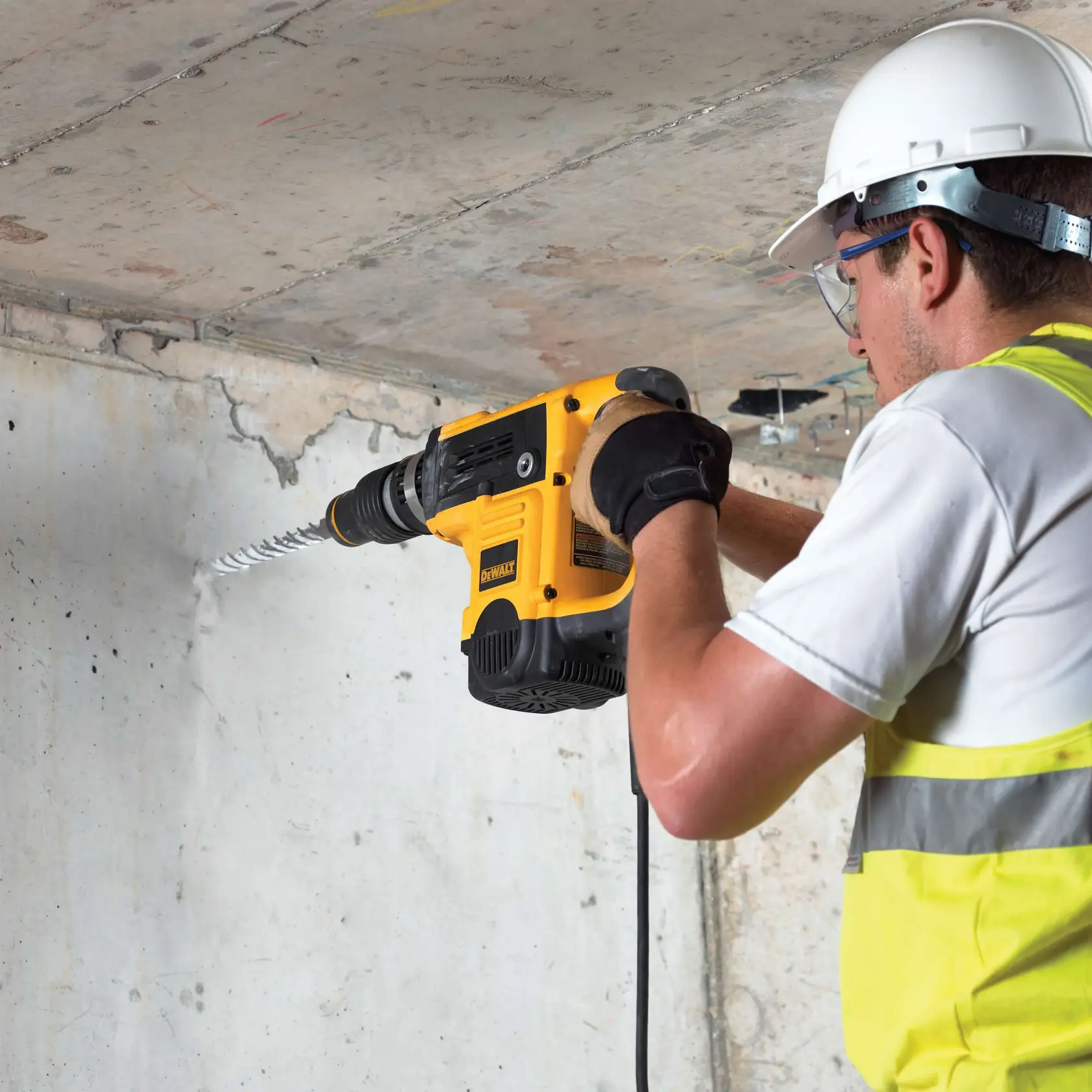 Person bohrt mit DEWALT-Bohrmaschine und DT9434 Bit in Betonwand, trägt Schutzkleidung.
