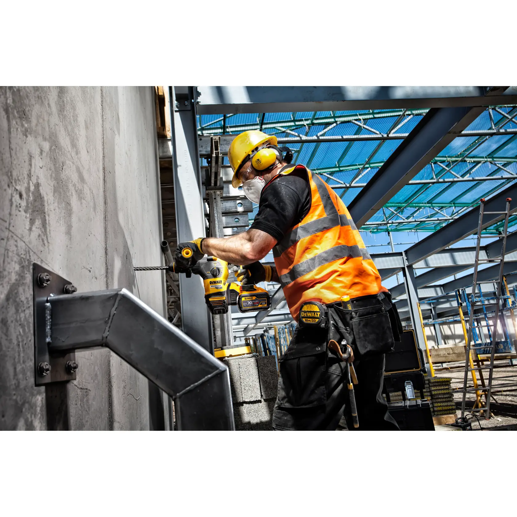 Trabajador con equipo de seguridad usa taladro DEWALT en pared de concreto en obra con vigas de acero.
