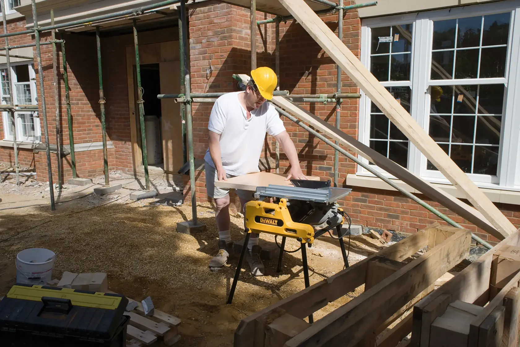 Trabajador usa una sierra DEWALT DW743N en obra exterior con tablones y andamios cercanos.