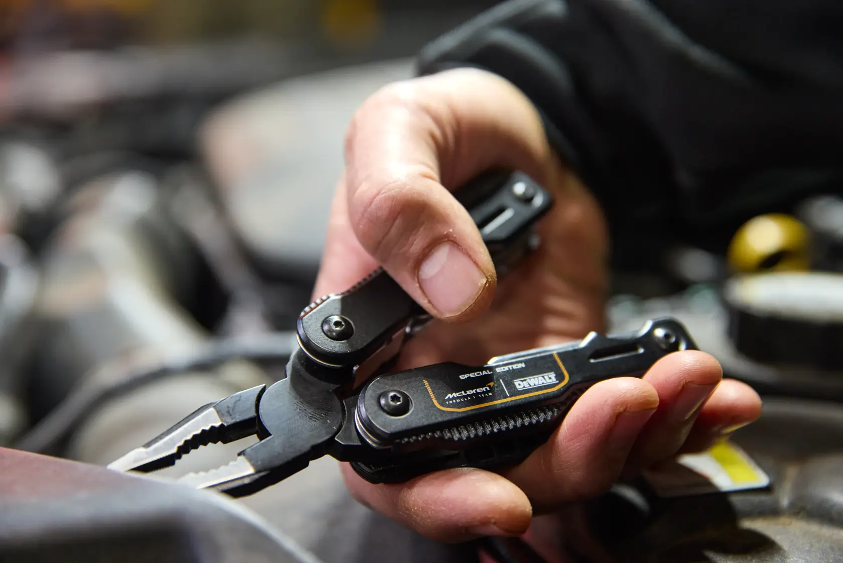 Mano sosteniendo un multitool negro DEWALT con alicates, usado para trabajos mecánicos en taller.