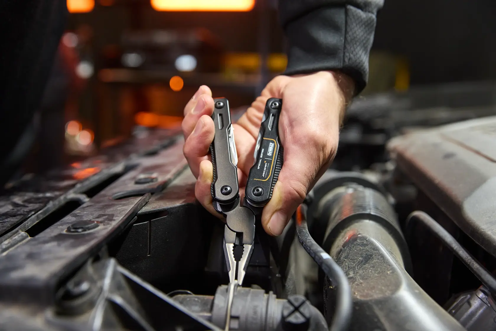 Mano usando pinzas multitool DEWALT para sujetar un cable en el motor de un coche.