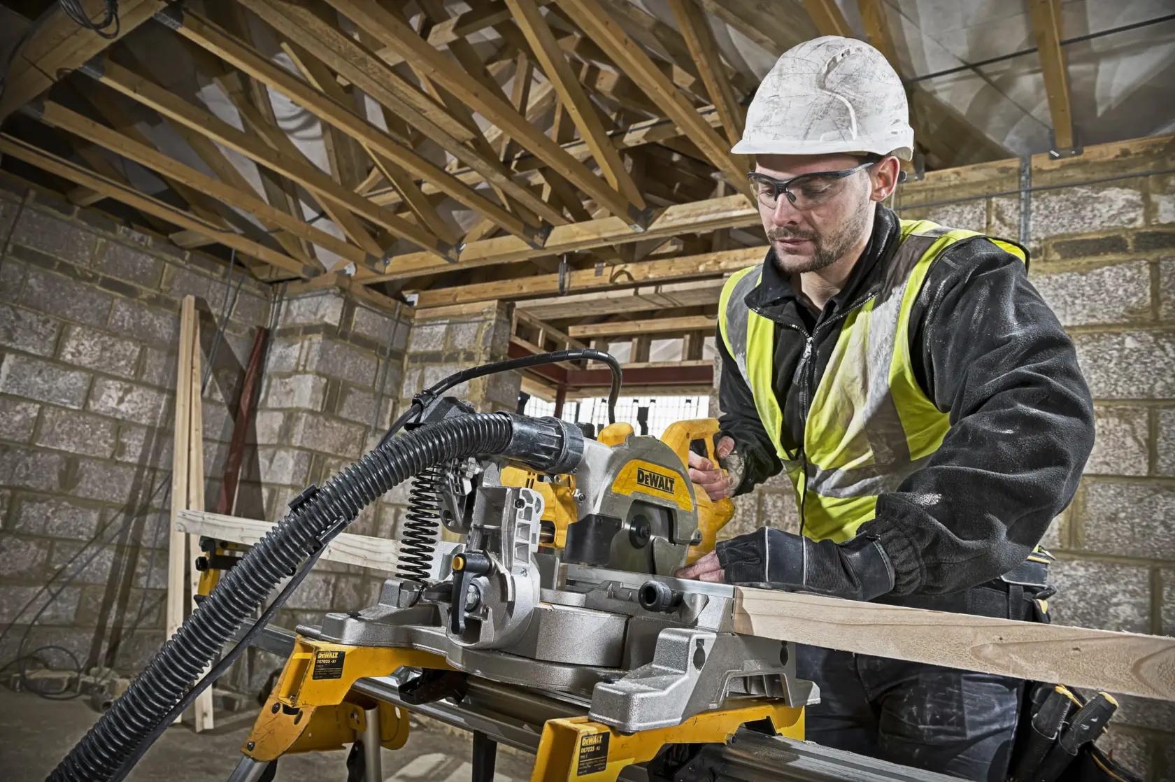 Trabajador corta madera con DEWALT DWS777 en obra. Lleva chaleco reflectante y protección.