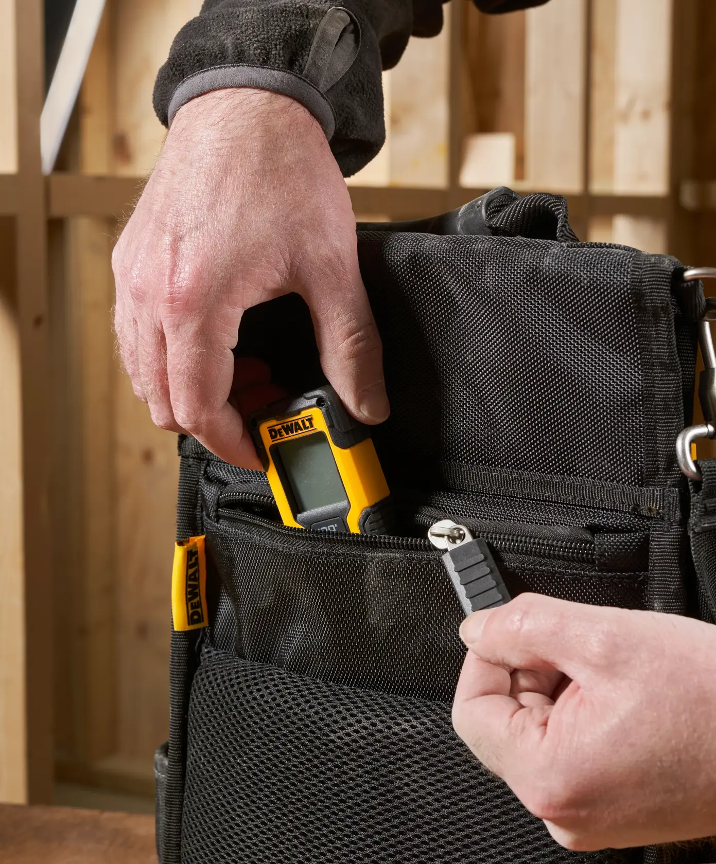 Mano guarda dispositivo DEWALT y punta en bolsillo negro con cremallera, en taller.