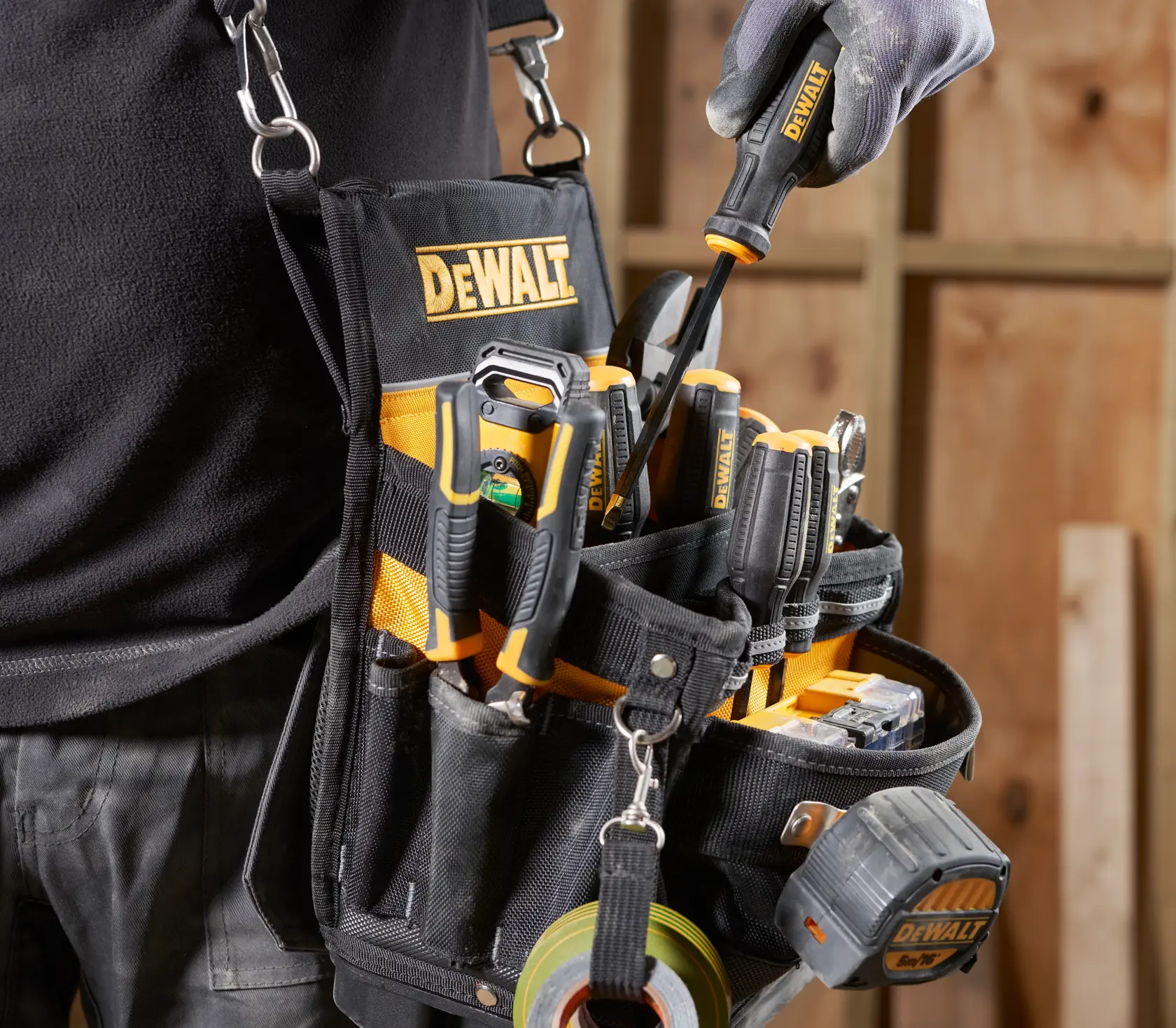 Cinturón de herramientas DEWALT con herramientas diversas y cinta métrica en taller de carpintería.